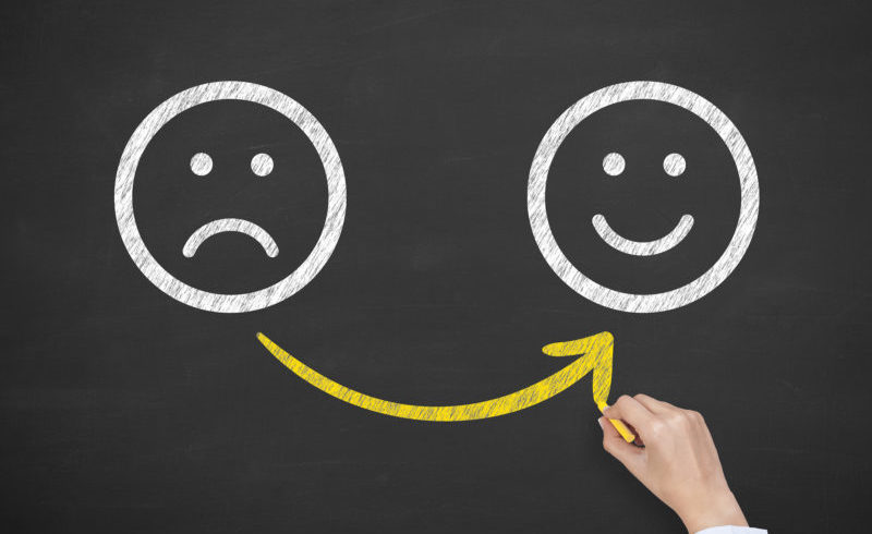 Hand drawing unhappy and happy smileys on blackboard