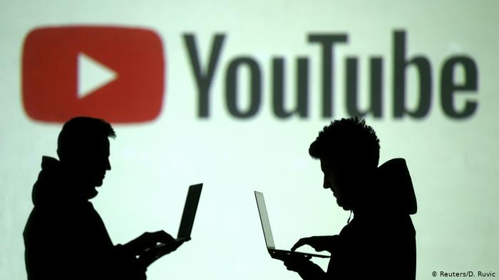 Фигуры двух мужчин, работающих с ноутбуками на фоне логотипа YouTube Забанят ли в России YouTube, Facebook и Instagram?
