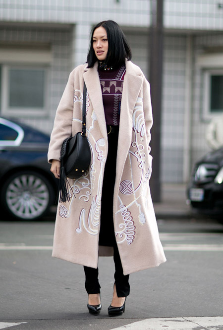 Девушка в черных брюках, кофта и светлое пальто с белым принтом, черные туфли и сумка