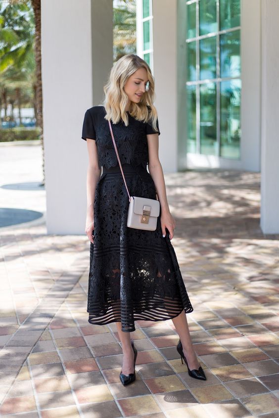 Модель в черном кружевном платье миди, туфли лодочки и белая сумочка
