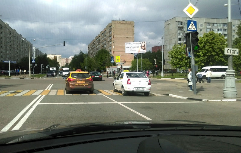 Перекресток Юбилейного проспекта и улицы Южной в городе Реутов Московской области. Если водитель желтого такси продолжит движение строго по прямой, то окажется на встречной полосе. Чтобы благополучно миновать перекресток, ему необходимо сместиться правее, но должен ли он при этом уступить дорогу коллеге справа? Перекресток