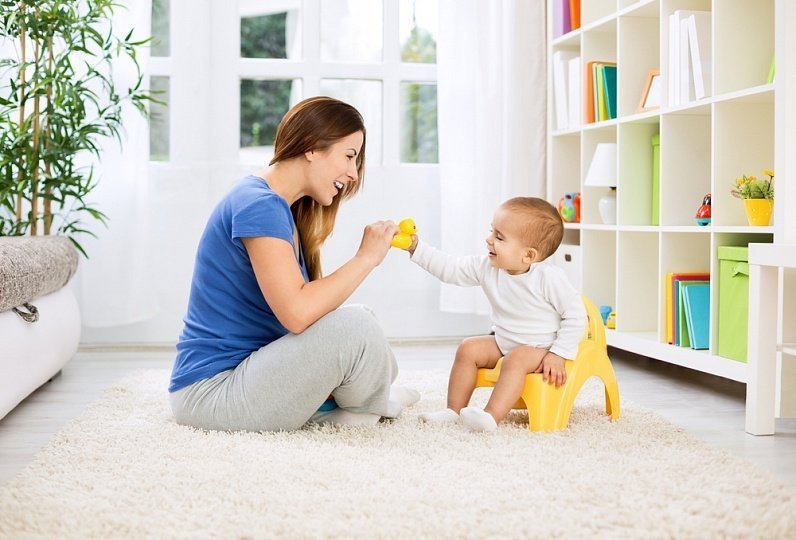 Мама с ребёнком, сидящим на горшке, держат жёлтую игрушку