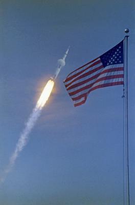 На этом снимке рекламного проспекта НАСА, сделанном 16 июля 1969 года, развевается американский флаг на фоне стартующего космического корабля Аполлон-11, совершившего первую посадку на Луну. Фото: NASA