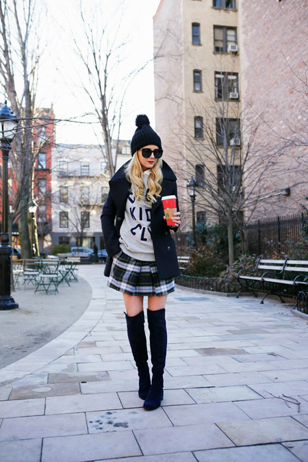 Девушка в черных высоких сапогах, клетчатой мини юбке, свишоте, укороченном пальто, черная шапка с помпоном