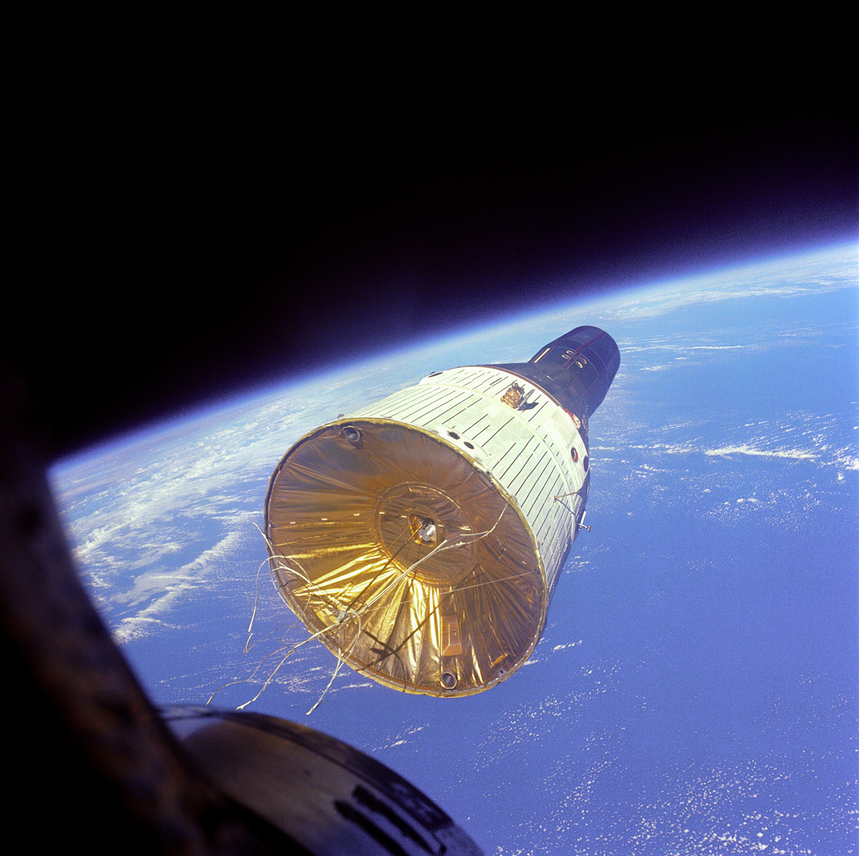 Вид на американский пилотируемый космический корабль «Джемини-7» с иллюминатора американского пилотируемого космического корабля «Джемини-6A». В момент сьёмки расстояние между объектами составляло 7 метров. На снимке «Джемини-7» находится на высоте 257 км над поверхностью Земли. (NASA on The Commons)