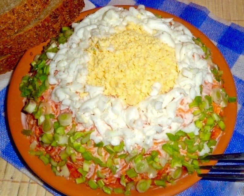 Салат из отварной горбуши, украшенный тертым яйцом и зеленым луком. 