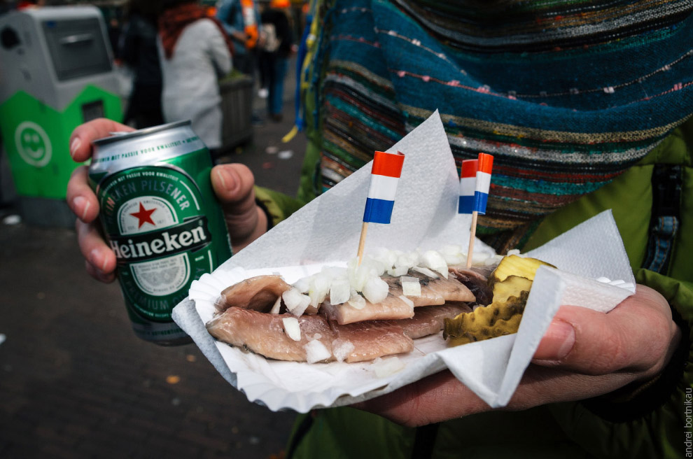 Hands hold a beer Heineken and a Dutch delicacy of herring with gherkins and onions.