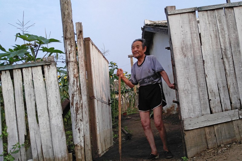 Пожилой мужчина выглядывает со своего двора в Туманганге жизнь, люди, путешествие, северная корея