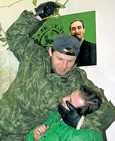 Александр МУЗЫЧКО, он же Сашко БИЛЫЙ, показывает на фоне портрета Джохара ДУДАЕВА, как он будет резать головы русским