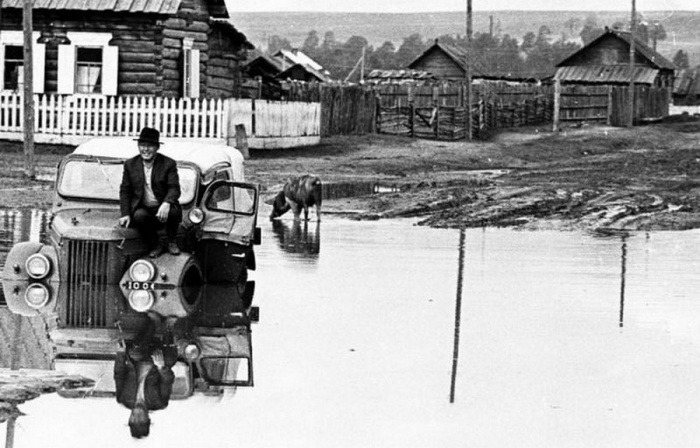 Черно-белое полотно с изображением машины и водителя, застрявшей посреди проселочной дороги в огромной луже. Черно-белое полотно с изображением машины и водителя, застрявшей посреди проселочной дороги в огромной луже.