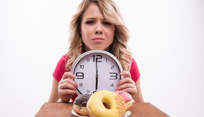 Time for diet slimming. Beautiful woman with clock keeps herself