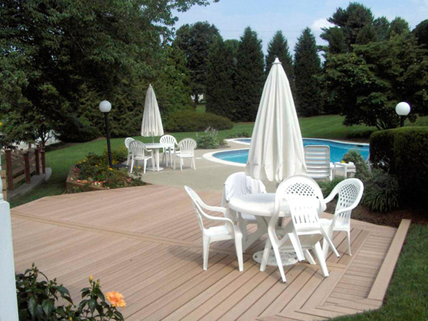 Deck in this back yard landscape design with poolside seating with white chairs and table and umbrella.