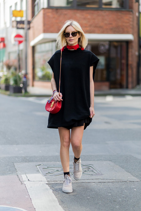 Модель в черном платье прямого покроя, красная сумочка и белые кеды