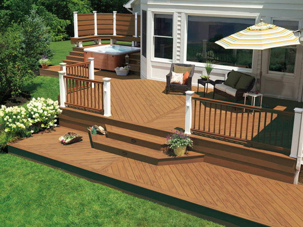 Multi level deck design in this backyard space with shaded seating area, railing, steps leading to yard, and hot tub on the side of the home.