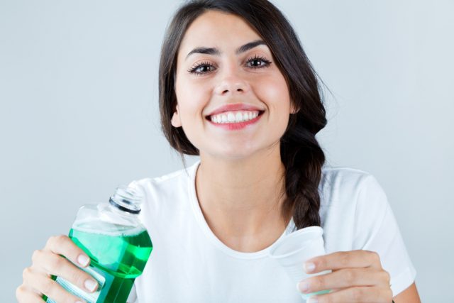Beautiful girl using mouthwash. Isolated on white.