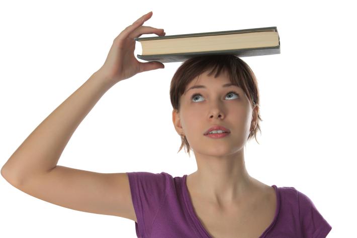 Beautiful girl the student holds the thick book on a head