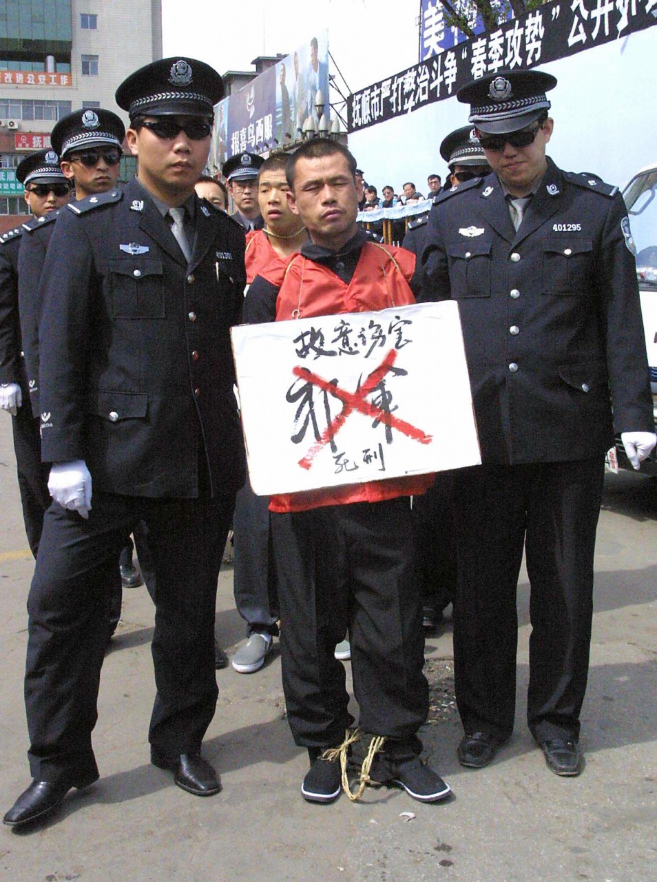 Заключенный в Шэньяне (Китай), которого собираются казнить, стоит с табличкой на шее. На верхней строке таблички - его преступление, ниже - зачеркнутое двумя красными линиями имя, указывающие, что заключенный приговорен к смерти. Фото: AFP/Getty Images