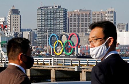 FILE PHOTO: Men wearing face masks watch as giant Olympic rings, which were temporarily taken down in August for maintenance amid the coronavirus disease (COVID-19) outbreak, are transported for reinstallation at the waterfront area at Odaiba Marine Park in Tokyo, Japan December 1, 2020. REUTERS/Kim Kyung-Hoon/File Photo