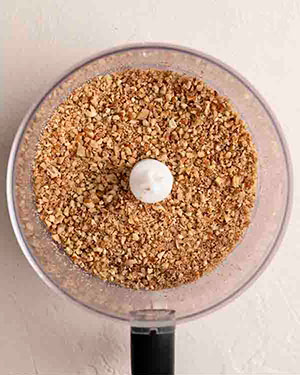 Добавьте сырые орехи пекан в кухонный комбайн и взбивайте, пока они не превратятся в грубые крошки.