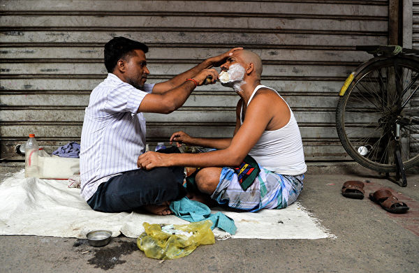 Парикмахер бреет клиента в придорожном магазине в старом квартале Нью-Дели 