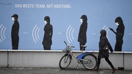 FILE PHOTO: A woman walks next to a poster reading "The best team. With distance." in front of a BMW factory as the spread of the coronavirus disease (COVID-19) continues in Munich, Germany, December 9, 2020. REUTERS/Andreas Gebert