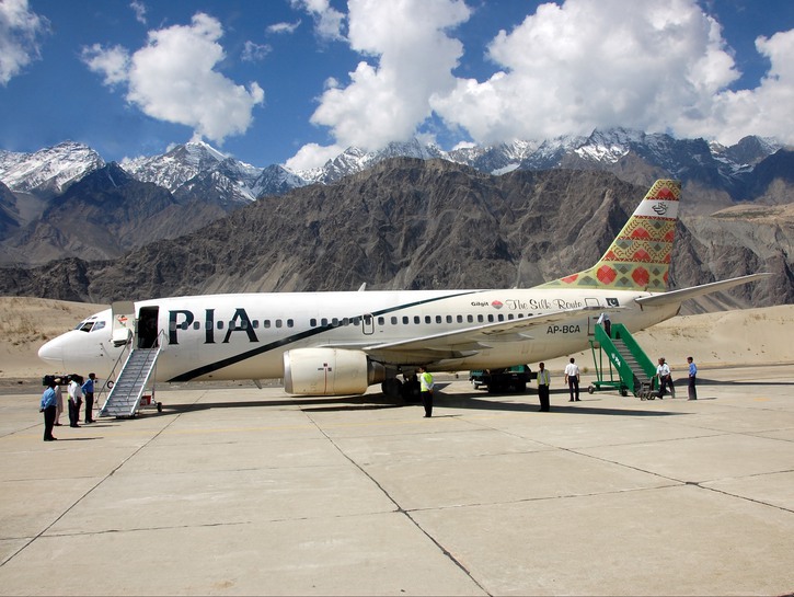 Pakistan International Airlines flight on tarmac with passengers boarding, mountains in the backgrou