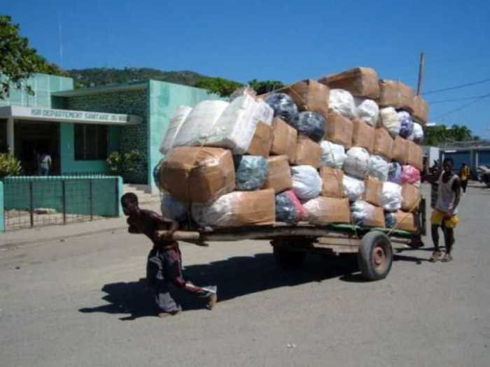Мужчина на двухколесной повозке перевозит огромное количество баулов.