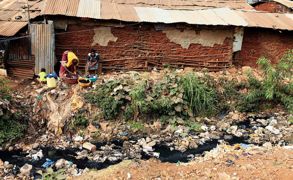 Стирка на берегу роскошного канала в трущобах в Найроби
