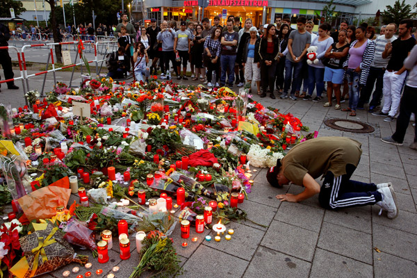 A man prays beside flowers laid in front of the Olympia shopping mall, where yesterday's shooting rampage started, in Munich, Germany July 23, 2016. REUTERS/Arnd Wiegmann     TPX IMAGES OF THE DAY      - RTSJCX2