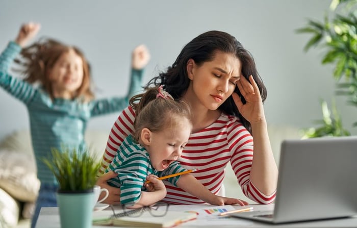 A stressed mom trying to work on her laptop while her kids distract her.