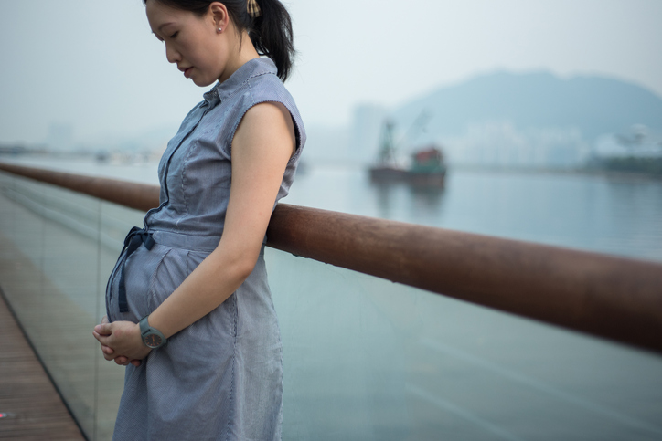 7 months pregnant women standing against a balustrade in a waterfront park along Victoria Harbour.