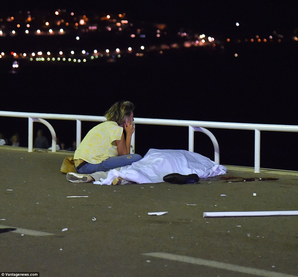 Bereft: A shocked woman in yellow sits on the phone next to the body of a loved-one, surrounded by debris,  as ISIS terrorists again struck in France, this time on Bastille Day, killing at least 84 