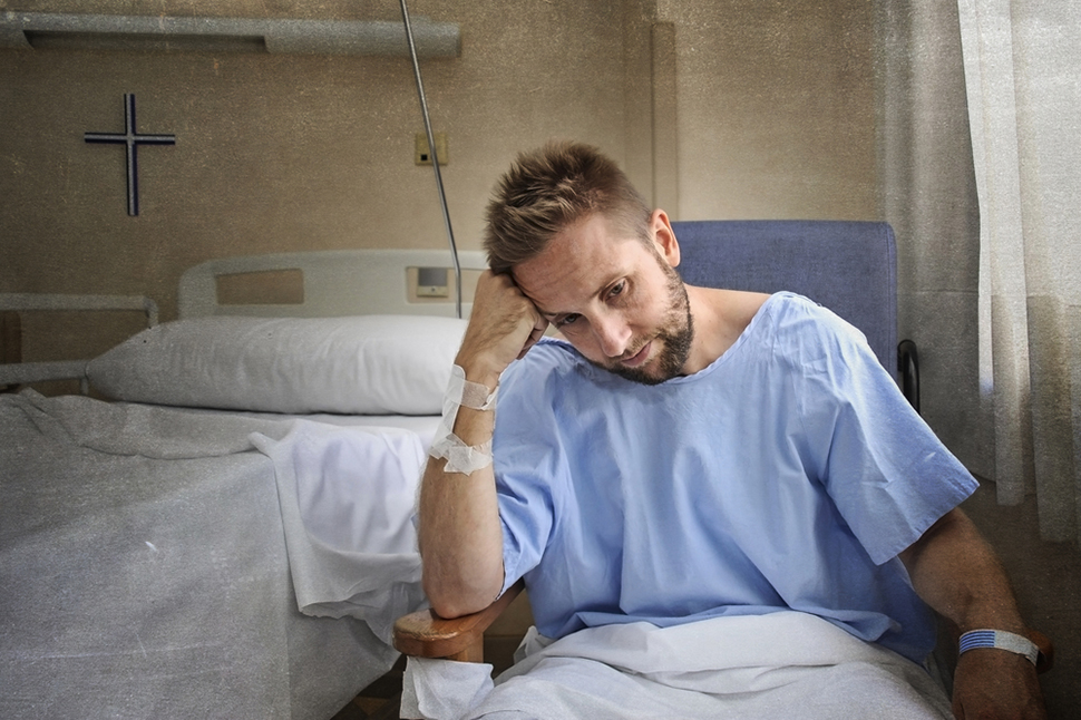 young injured man in hospital room sitting alone in pain worried