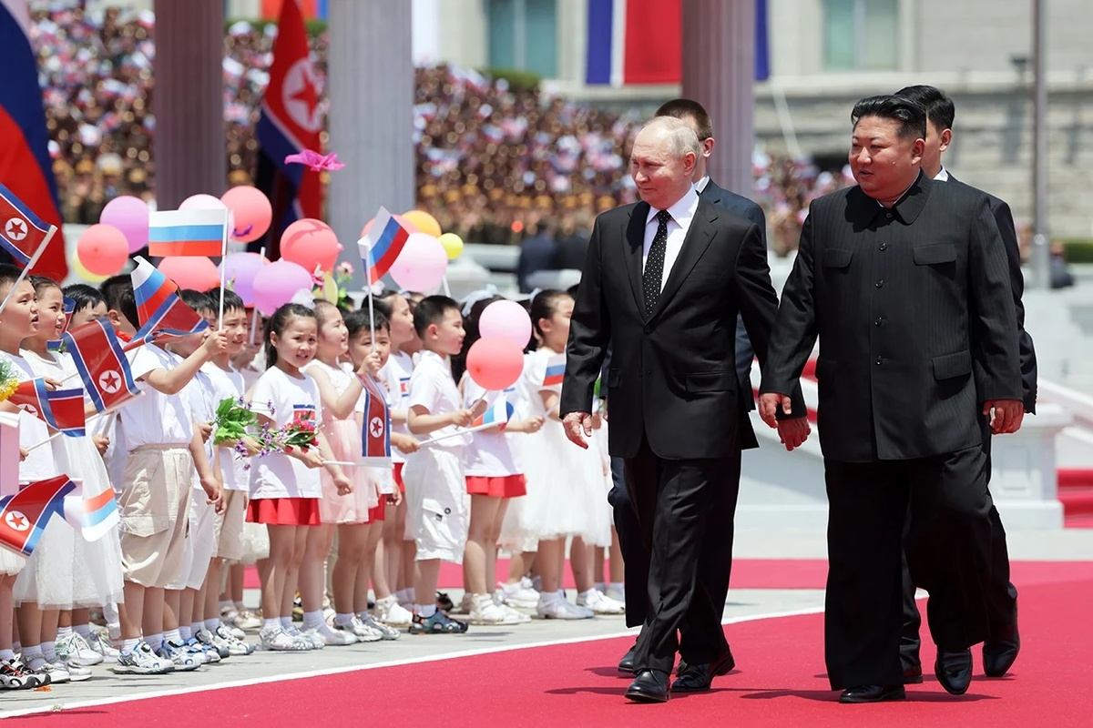 На фотографии изображены Владимир Путин и Ким Чен Ын, идущие вместе на торжественной церемонии. Справа от них северокорейские дети приветствуют их, держа в руках воздушные шарики и флажки России и Северной Кореи
