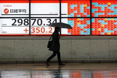 A man holding an umbrella walks in front of an electric board showing Nikkei index a brokerage in Tokyo, Japan February 15, 2021. REUTERS/Kim Kyung-Hoon
