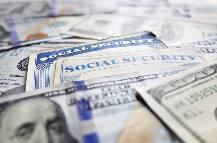 Two Social Security cards laid atop a messy pile of one hundred dollar bills.