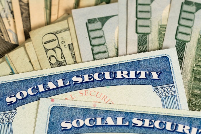 Two Social Security cards sitting atop a pile of fanned-out U.S. currency.