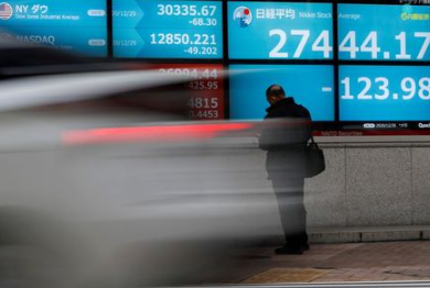 FILE PHOTO: A man stands in front of a screen displaying Nikkei share average and the world's stock indexes outside a brokerage, amid the coronavirus disease (COVID-19) outbreak, in Tokyo, Japan December 30, 2020. REUTERS/Issei Kato