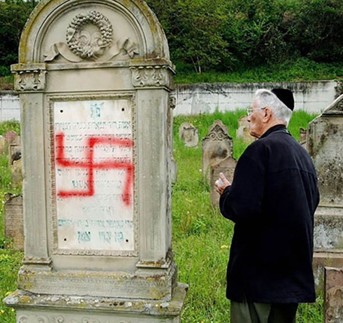 An unidentified member of the Jewish community looks at a swastika painted on a headstone at a Jewish cemetery in Herrlisheim, eastern France, Friday, April 30, 2004. About 100 headstones have been desecrated in the cemetery and the French government quickly condemned the attack. In the past few years, France has suffered a wave of violence against Jewish schools, synagogues and cemeteries that coincided with new fighting in the Middle (AP Photo/Gil Michel)