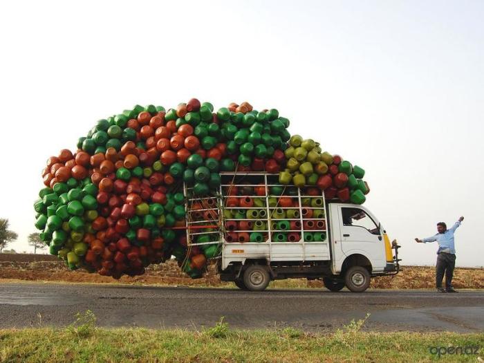 Маленький индийский грузовик с кузовом, переполненным пластиковыми кувшинами.