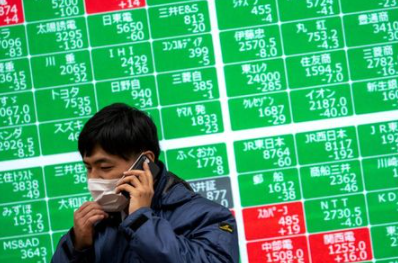 FILE PHOTO: A man wearing a protective face mask, following an outbreak of the coronavirus, talks on his mobile phone in front of a screen showing the Nikkei index outside a brokerage in Tokyo, Japan, February 26, 2020. REUTERS/Athit Perawongmetha/File Photo