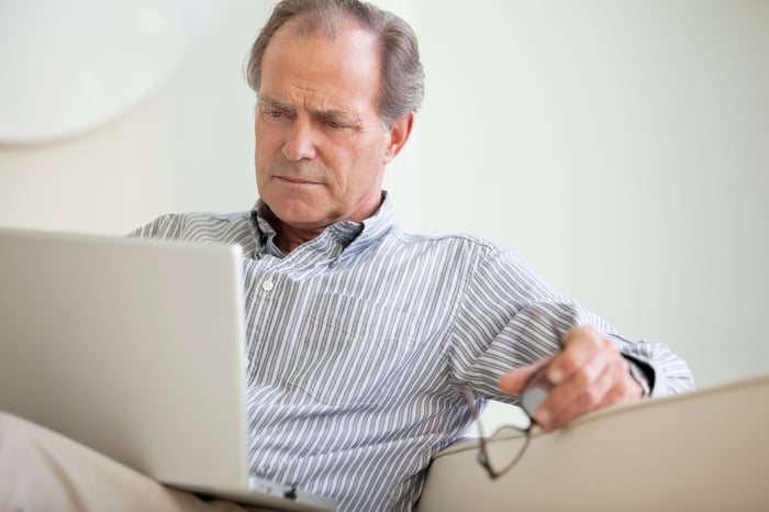 A person sitting on a couch who's critically reading content from an open laptop on their lap.