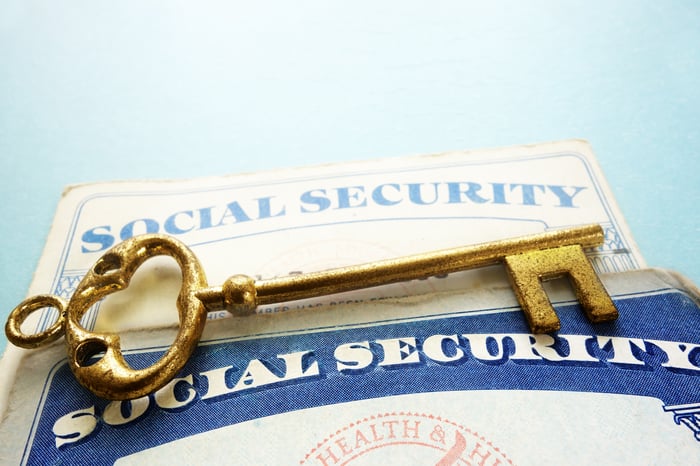 A gold-colored key symbolically placed atop two Social Security cards of varying ages. 