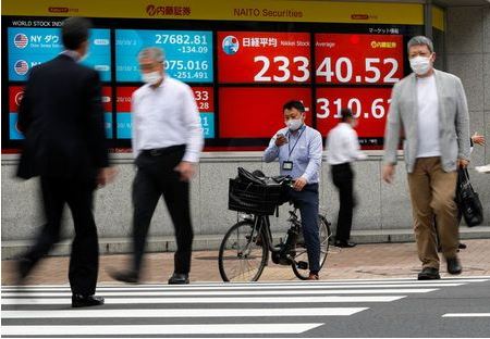 Passersby wearing protective face masks walk past a screen displaying Nikkei share average and world stock indexes outside a brokerage, amid the coronavirus disease (COVID-19) outbreak, in Tokyo, Japan October 5, 2020. REUTERS/Issei Kato