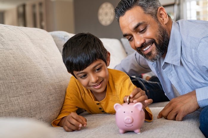 Parent teaching child how to save money in a piggy bank. 