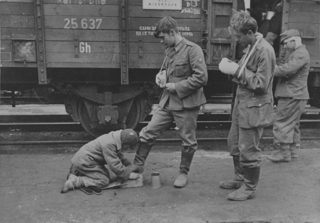 Подросток чистит сапоги раненому немецкому солдату на оккупированной железнодорожной станции в СССР. 1943 г.