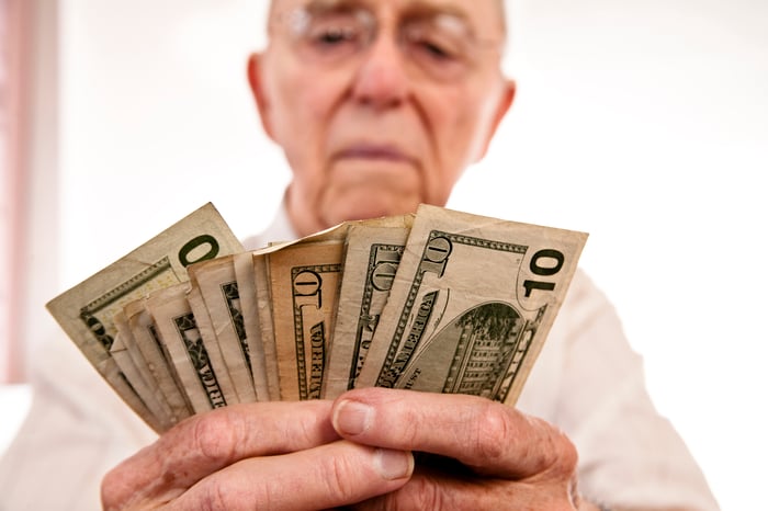 A seated person counting an assortment of cash bills held in their hands. 