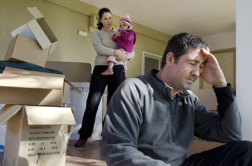 Young parents and their daughter stand beside cardboard boxes outside their home. Concept photo illustrating divorce, homelessness, eviction, unemployment, financial, marriage or family issues.