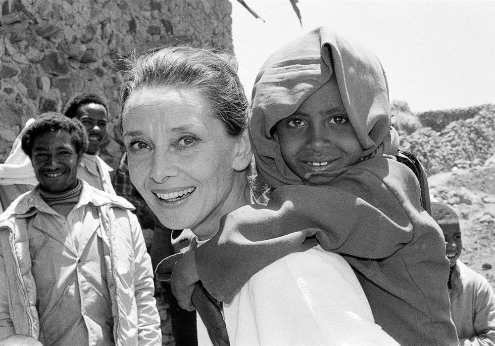 UNICEF Goodwill Ambassador Audrey Hepburn smiles as she carries a child on her back, in the northern town of Mehal Meda in Shoa Province. Ms. Hepburn was visiting a food distribution centre in the town. In 1988, internationally known film actor and UNICEF Goodwill Ambassador Audrey Hepburn travelled to Ethiopia on her first official UNICEF mission, to raise awareness of the impact of the continuing drought on the country's children and women. During her trip, sponsored by the United States Committee for UNICEF, Ms. Hepburn visited UNICEF-assisted health clinics and supplementary feeding programmes, 'food-for-work' projects, an income-generating project and an orphanage for children who have been abandoned or orphaned in this region during the drought. Ms. Hepburn was appointed a UNICEF Goodwill Ambassador on 9 March of this year.