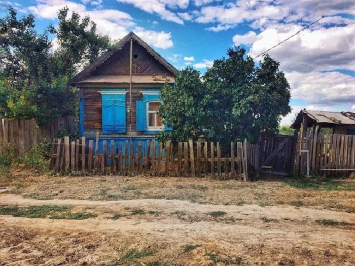 Маленький деревянный домик с окрашенными синими ставнями притаился за самодельным редким заборчиком.